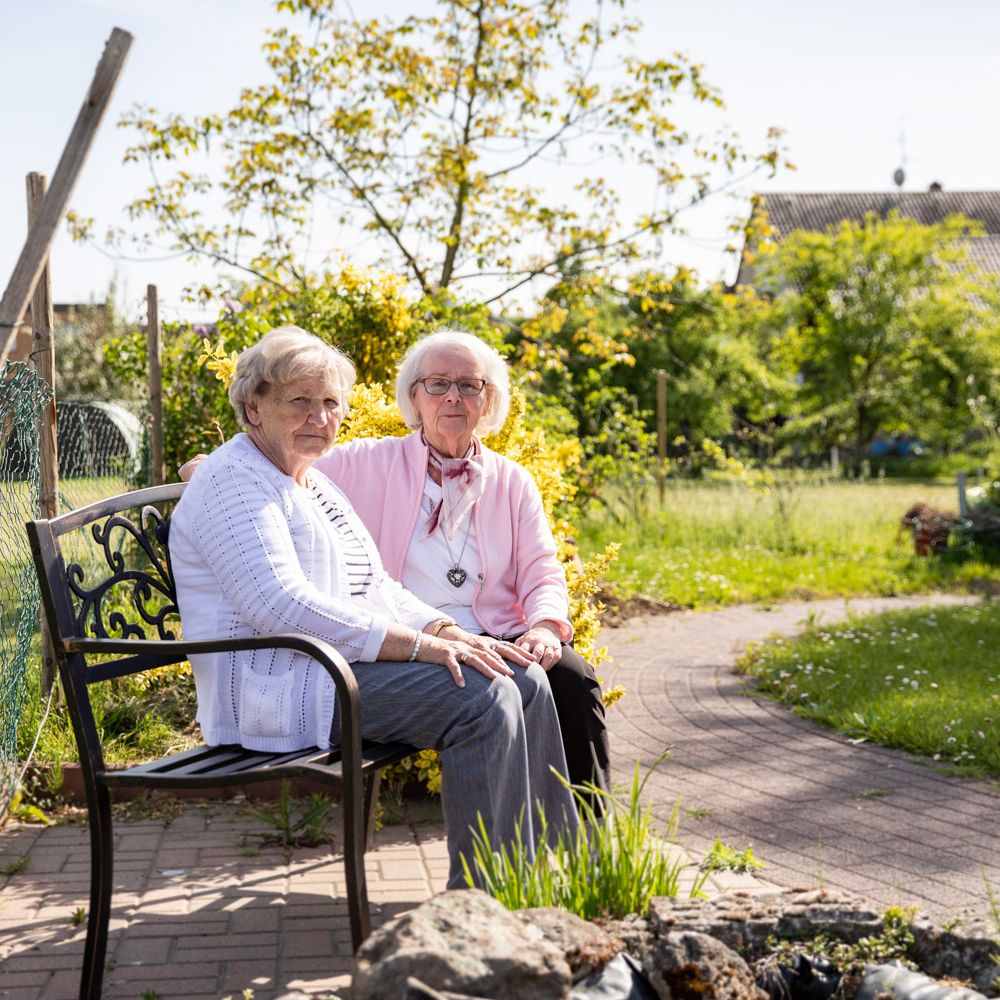 Zwei Klientinnen sitzen im Garten auf einer Bank