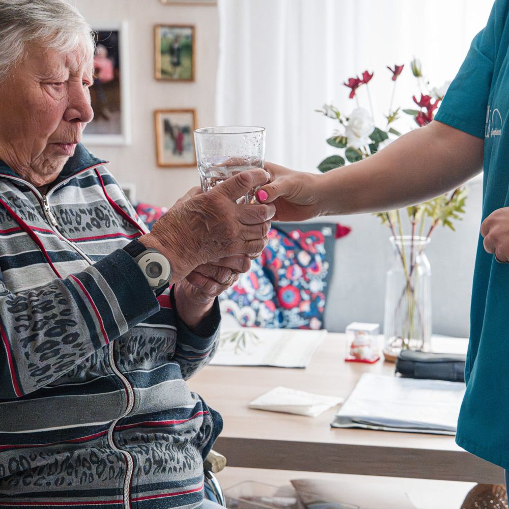 Mitarbeiterin reicht einer Frau ein Glas Wasser